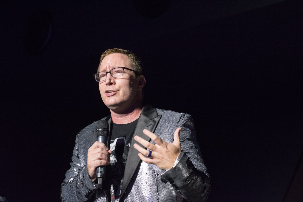 Tim talks enthusiastically into a microphone while wearing a shiny silver sequin jacket